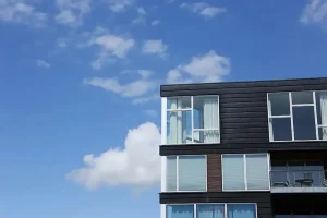 Et hus med en sort facade og store vinduer mod en baggrund af en blå himmel med et par skyer.